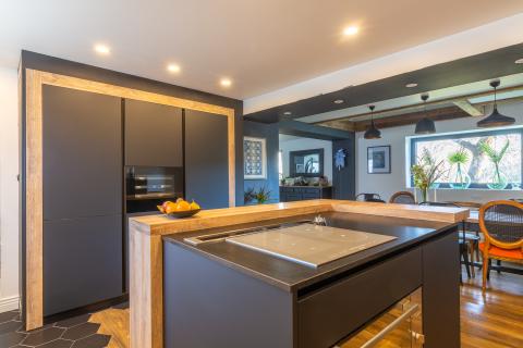 Le choix d'une cuisine noire mate crée une ambiance contemporaine et sophistiquée, en parfaite harmonie avec le style loft industriel. Les meubles au fini mat apportent une touche de modernité tout en minimisant les reflets indésirables. Les éléments en bois, tels que les étagères ou les tabourets de bar, ajoutent une chaleur naturelle à l'ensemble de la pièce et créent un contraste agréable avec le noir mat.